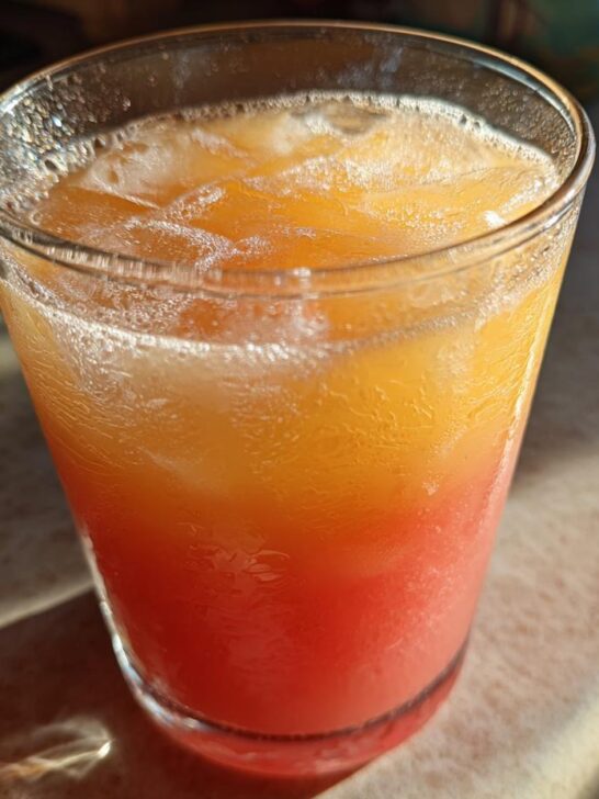 Close-up of a layered Pineapple Watermelon Mocktail with ice cubes in a clear glass, showing orange and red layers.