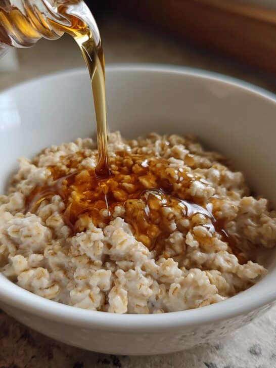Close-up of maple syrup being poured over a bowl of creamy Maple Brown Sugar Oatmeal.