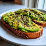Two slices of toasted bread topped with mashed avocado and everything bagel seasoning for Saturday Morning Everything Avocado Toast.