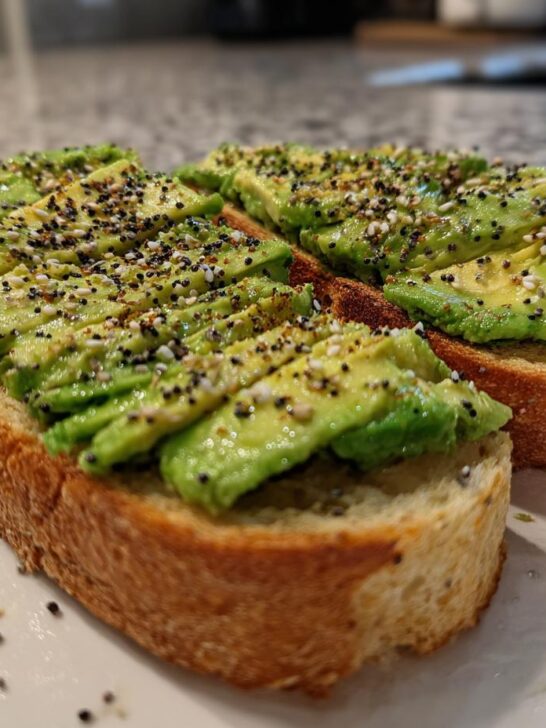 Two slices of toasted bread topped with fanned avocado slices and everything bagel seasoning for Saturday Morning Everything Avocado Toast.