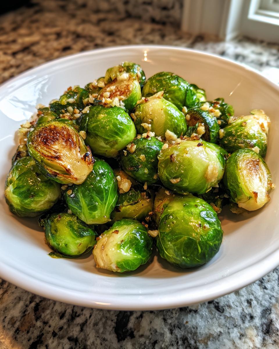A close-up of bright green, glistening Sauteed Brussel Sprouts topped with minced nuts or garlic, served in a white bowl.