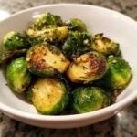 Close-up of bright green and caramelized Sauteed Brussel Sprouts seasoned with garlic and herbs in a white bowl.