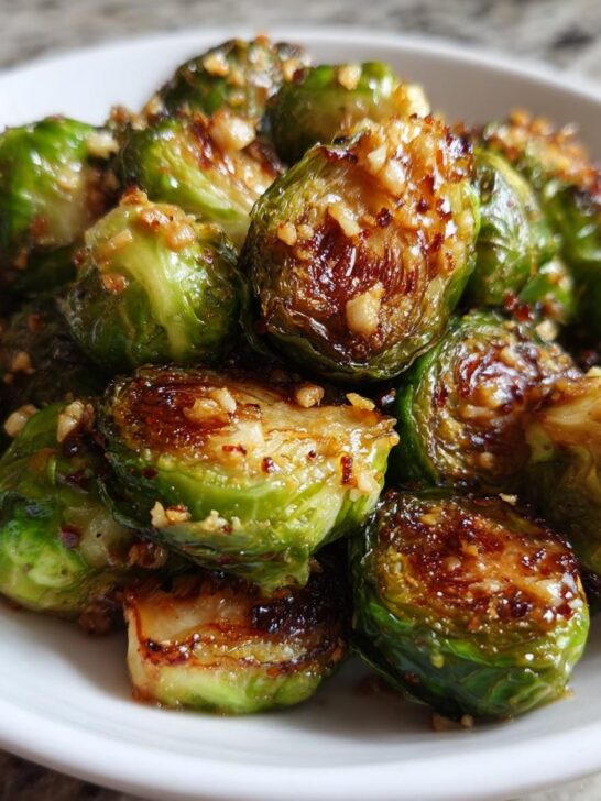 Close-up of bright green, caramelized Sauteed Brussel Sprouts tossed with minced garlic in a white bowl.