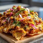 A close-up, appetizing shot of Sheet Pan Buffalo Chickpea Nachos piled high with melted cheese, seasoned chickpeas, and red onion.