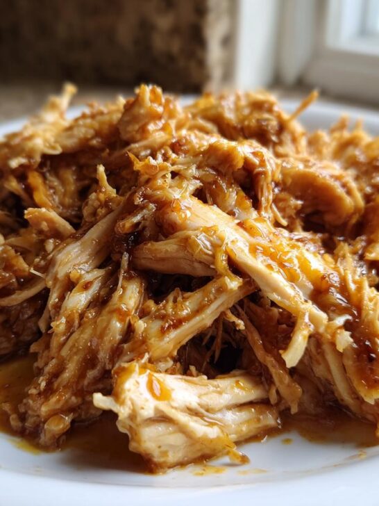 Close-up of shredded Crock Pot Honey Garlic Chicken coated in a thick, glossy honey garlic sauce, served on a white plate.