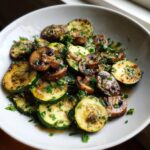 Close-up of saut&eacute;ed Skillet Zucchini Mushrooms topped with garlic and fresh parsley in a white bowl.