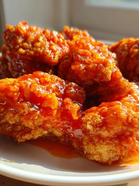 Close-up of crispy fried chicken pieces generously coated in a shiny, bright orange Southern hot honey glaze.