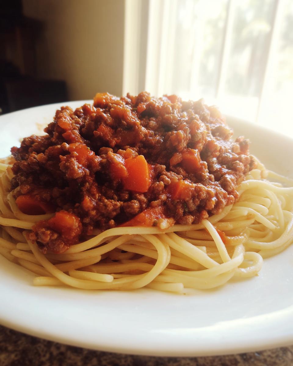 A plate of spaghetti topped generously with rich Homemade Bolognese Sauce, featuring visible chunks of carrot.