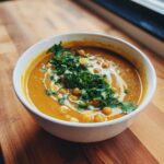 A close-up of Spicy Curry Pumpkin Soup With Chickpeas, topped with a swirl of cream, whole chickpeas, and fresh cilantro.