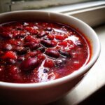 Close-up of a white bowl filled with rich, deep red Spicy Vegan Chili featuring kidney beans.