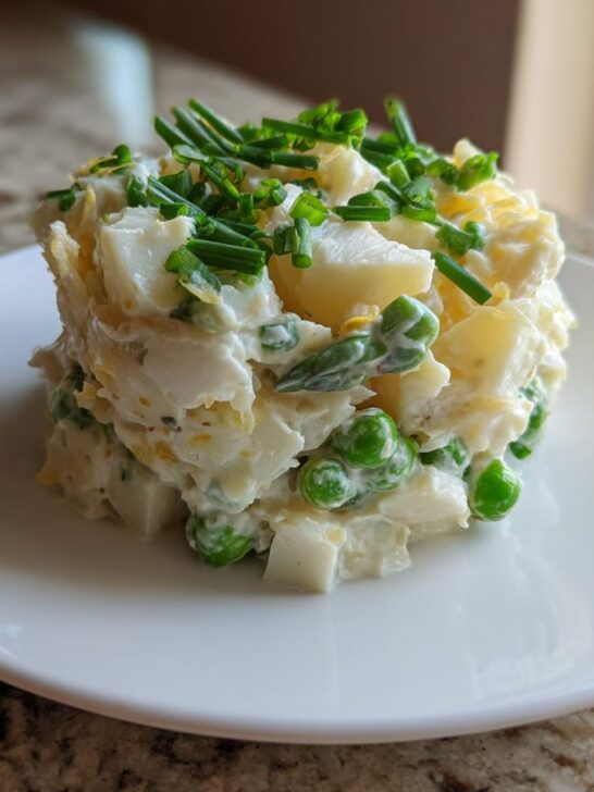 A molded serving of creamy Spring Vegetable Potato Salad featuring potatoes, peas, and topped with fresh chives.