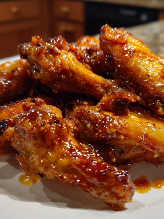 A pile of perfectly glazed, Sticky Peach Chicken Wings glistening with sauce on a white plate.