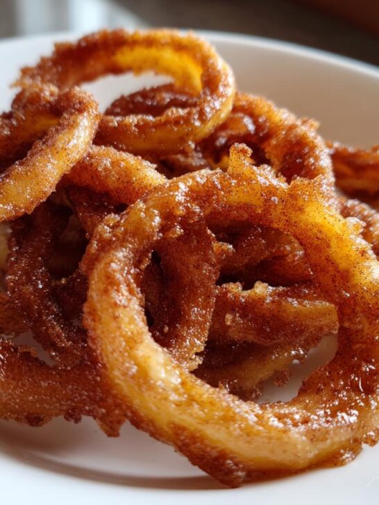 Close-up of several golden brown, fried Apple Rings dusted heavily with cinnamon sugar on a white plate.