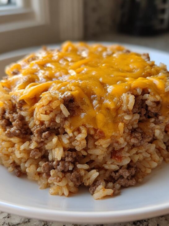 A serving of Taco Beef Rice Skillet molded on a white plate, topped with melted cheddar cheese.