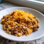 A close-up serving of Taco Beef Rice Skillet topped generously with melted shredded cheddar cheese.