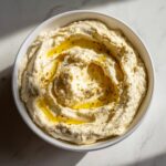 Overhead view of a white bowl filled with The Best Classic Hummus, swirled and drizzled with olive oil and spices.