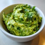 Close-up of The Best Guacamole, chunky and bright green, topped with fresh cilantro in a small white bowl.