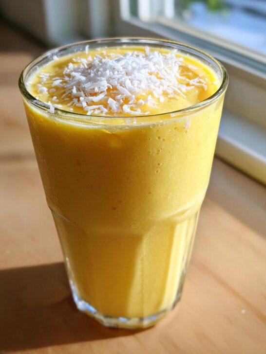 A vibrant yellow Tropical Pineapple Coconut Smoothie topped with shredded coconut flakes in a glass.