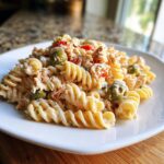 Close-up of creamy Tuna Pasta Salad With Pimiento Stuffed Olives featuring rotini pasta and green olives on a white plate.