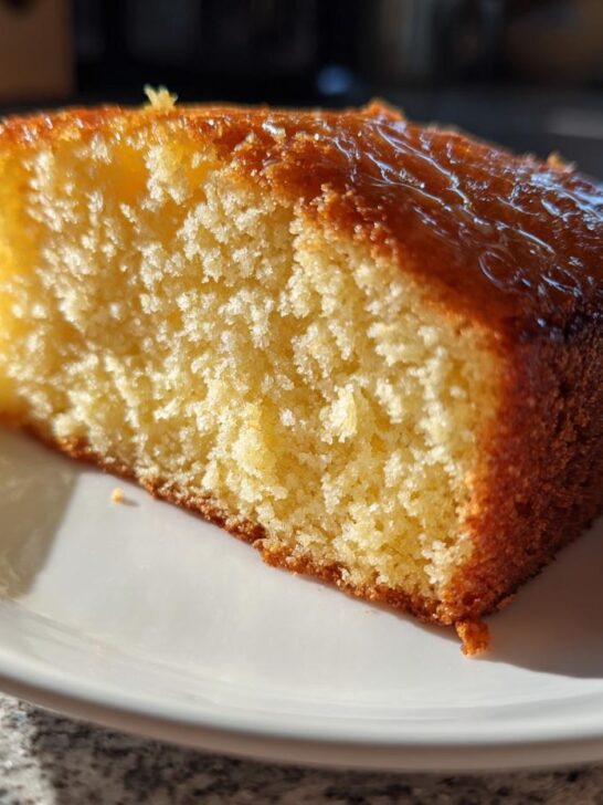 Close-up of a moist slice of Two Ingredient Lemon Cakes with a shiny glaze topping, sitting on a white plate.