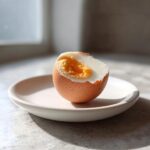 A soft-boiled egg, halved to show a jammy yolk, ready for eating after Preparing Boiled Eggs Using An Air Fryer.