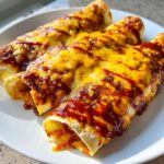 Three golden brown cheese enchiladas topped with melted cheddar and a drizzle of red sauce, ready to eat.
