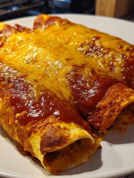 Three freshly cooked cheese enchiladas, covered in red sauce and melted cheddar, ready to eat.