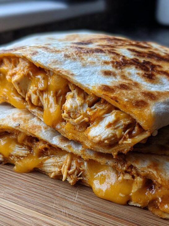 Two halves of a golden, crispy chicken quesadilla overflowing with shredded chicken and melted orange cheese, ready for eating.