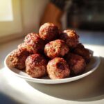 A mound of perfectly browned, cooked frozen meatballs piled high on a white plate, ready to eat.