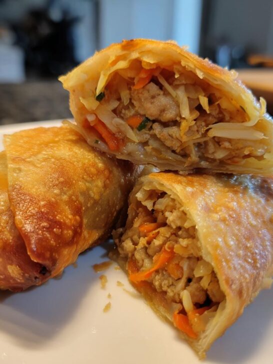 Close-up of crispy Air Fryer Pork Egg Rolls, one cut open showing pork and shredded vegetables inside.