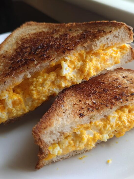 Two halves of a toasted sandwich filled with bright orange, cheesy cauliflower mixture, representing the Cauliflower Grilled Cheese.