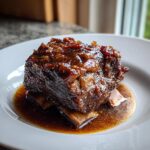 A close-up of tender Apple Cider Braised Short Ribs coated in a thick, glossy glaze, served on a white plate.