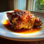 Close-up of a piece of Apple Cider Vinegar Braised Chicken with a rich, glossy, dark orange glaze sitting in sauce.