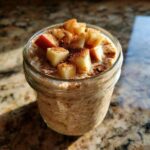 A glass jar filled with Apple Cinnamon Overnight Oats, topped with diced apples and cinnamon spice.