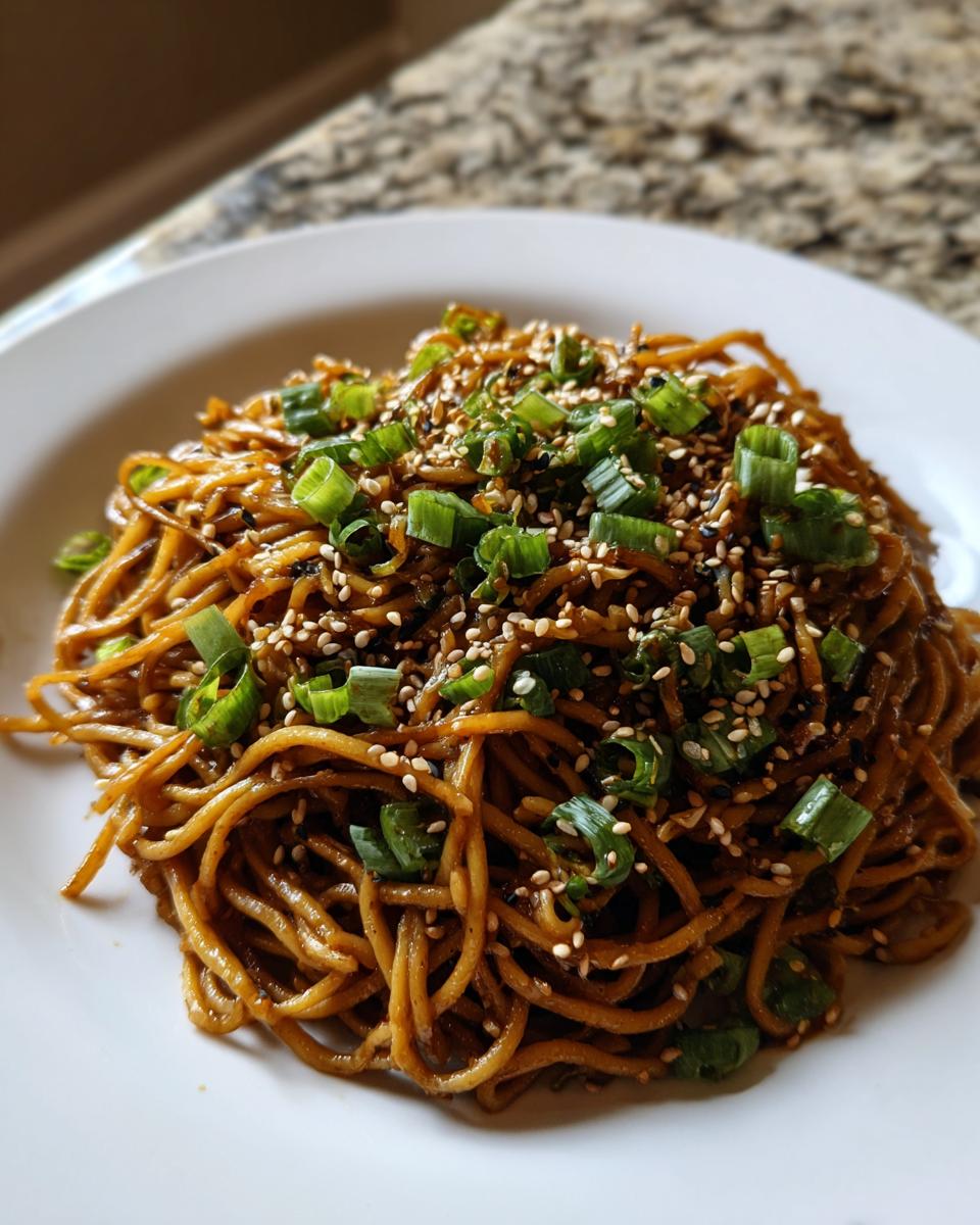 A close-up of a mound of glossy Asian Sesame Noodles topped with chopped green onions and toasted sesame seeds.