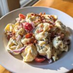 A close-up of a creamy Bacon Ranch Tortellini Salad topped with crispy bacon pieces and red onion.