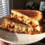 Two halves of a Baked BBQ Chicken Grilled Cheese Dairy Free sandwich showing melted dairy-free cheese and shredded chicken.