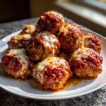 A pile of juicy Baked Chicken Parmesan Meatballs topped with melted mozzarella cheese and marinara sauce.