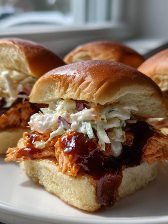 Four delicious Baked Salmon Sliders With BBQ Jerk Sauce topped with creamy coleslaw, served on a white plate.