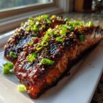 Two glistening fillets of Baked Teriyaki Salmon covered in dark glaze, sesame seeds, and sliced green onions.