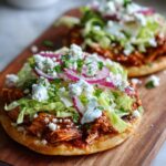 Close-up of a delicious Bbq Chicken Tostadas topped with lettuce, red onion, cotija cheese, and crema.