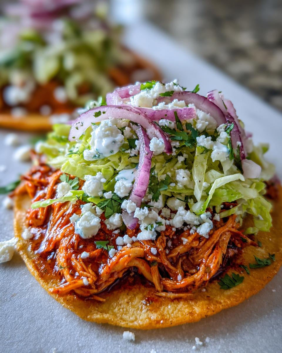 Close-up of a Bbq Chicken Tostada topped with shredded lettuce, red onion, and crumbled white cheese.