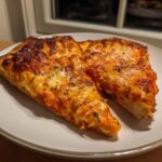 Two generous slices of Best Homemade Vodka Pizza with bubbly, browned cheese and herbs on a light plate.