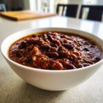 Close-up of a white bowl filled with rich, thick Best Mamas Beer Chili Slow Cooker Recipe featuring ground meat and kidney beans.