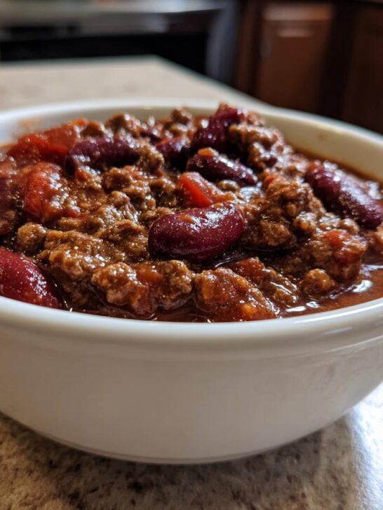 Close-up of a white bowl filled with hearty Best Mamas Beer Chili Slow Cooker Recipe, featuring ground meat and kidney beans.