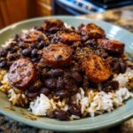 Close-up of Black Beans And Rice With Sausage served over white rice in a light green bowl.