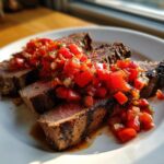 Slices of perfectly cooked Brazilian BBQ Steak topped generously with bright red Vinagrete Sauce on a white plate.