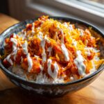 A close-up of a Buffalo Chicken Bowl featuring white rice topped with saucy chicken, shredded cheddar cheese, and a drizzle of white ranch dressing.