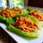 Four servings of shredded, orange-sauced Buffalo Chicken Lettuce Wraps arranged on a white platter.