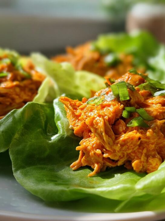 Three servings of vibrant orange Buffalo Chicken Lettuce Wraps topped with sliced green onions on a light blue plate.